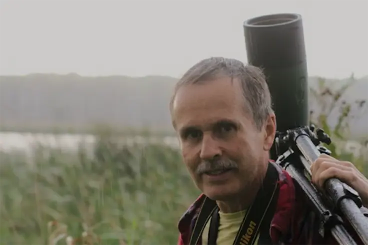 A man near a wetland with a camera on a tripod